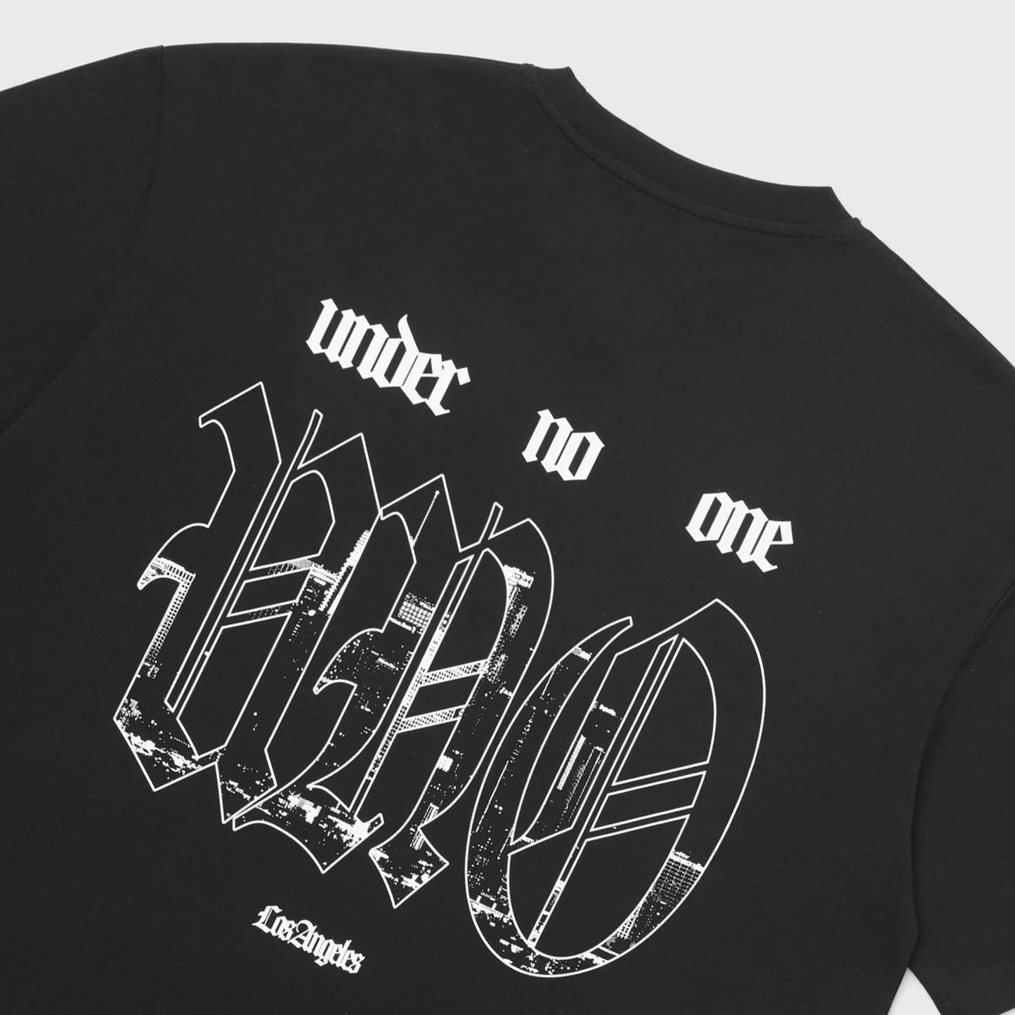 Black t-shirt back featuring 'under no one' text above large gothic-style 'UNO' logo with distressed city skyline pattern inside letters, and 'Los Angeles' text below, all in white.